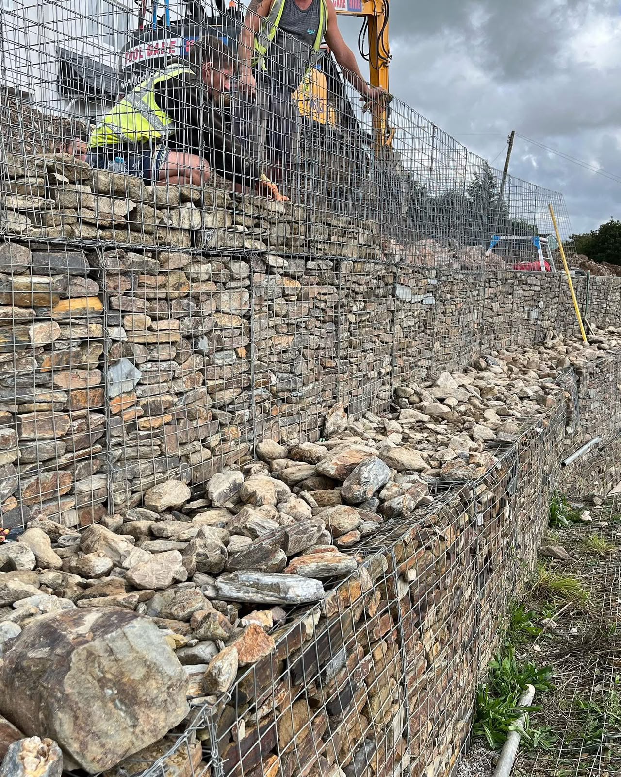 Operatives building tiered stone-filled gabion baskets on a residential estate in Calstock