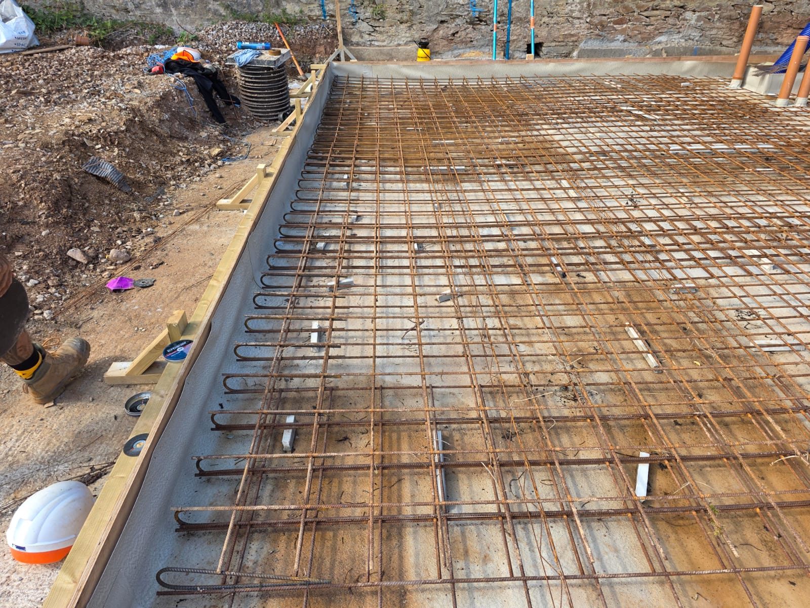 Reinforced concrete base by CC Construction Ltd: steel mesh, formwork and service pipes set ready for a slab pour in Cornwall